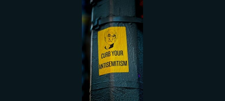 a sticker on the side of a pole that says curb your antisemitism by Jon Tyson, Unsplash licence, https://unsplash.com/photos/a-sticker-on-the-side-of-a-pole-that-says-curb-your-antisemit-iCP8fi7MX0c