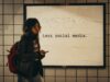 a woman standing in front of a sign that says less social media by Jon Tyson, unsplash license, https://unsplash.com/photos/a-woman-standing-in-front-of-a-sign-that-says-less-social-media-e1xl7iby_Ug